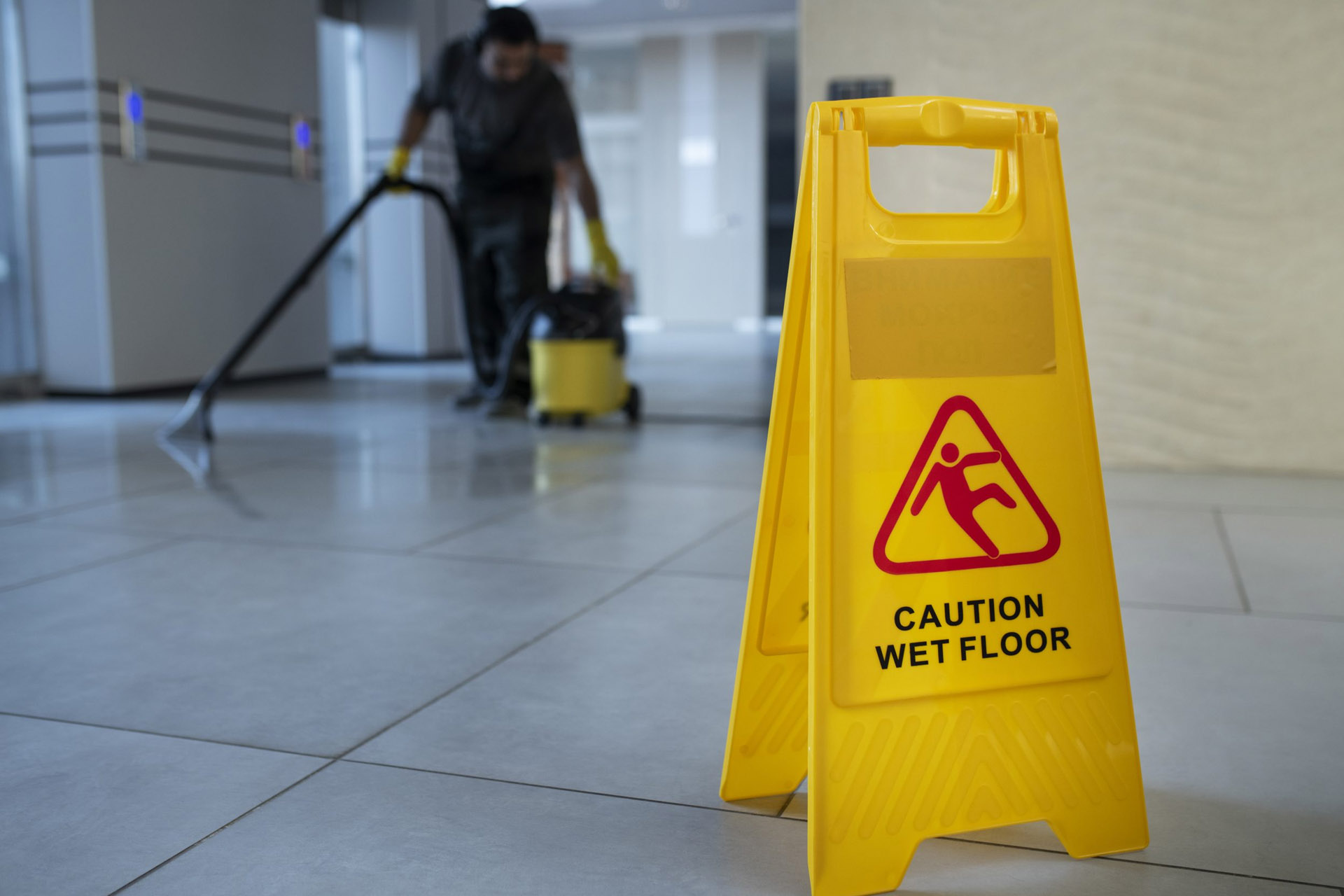 A yellow caution sign in front of a man cleaning the floor.