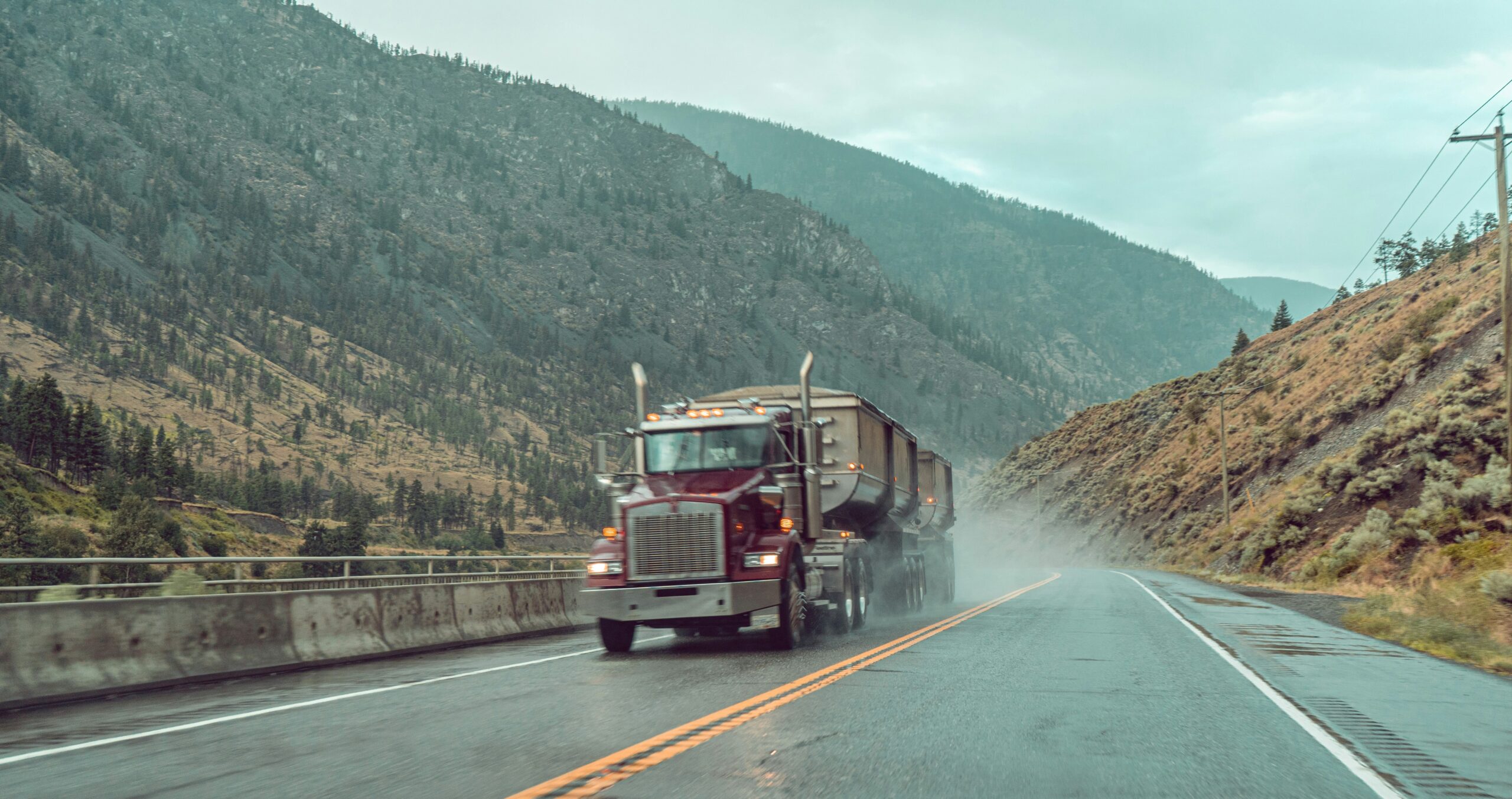 A semi truck driving down the road near some mountains.